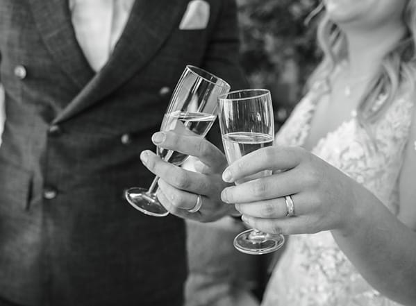 Zwart-wit foto waarbij een bruidspaar twee champagneglazen vasthoudt.