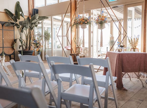 Trouwzaal met mooi versierde witte stoelen op een rij en het trouwbordeel daarvoor.