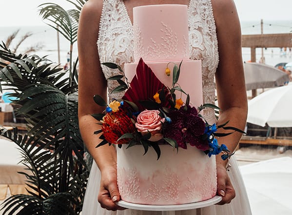 Prachtige roze trouwtaart met bloemenstuk erop.